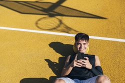 Male basketball player using his smartphone resting after training