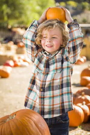 Little Boy Holding His Pumpkin at a Pumpkin Patch Above His Head