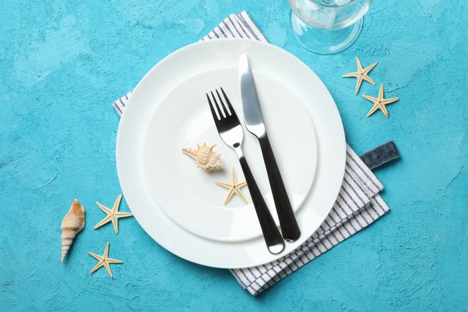 Table setting with seashells and starfishes on turquoise background, top view