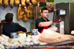 Man in butcher shop serving a customer at register with colleague behind the counter 5llEN5
