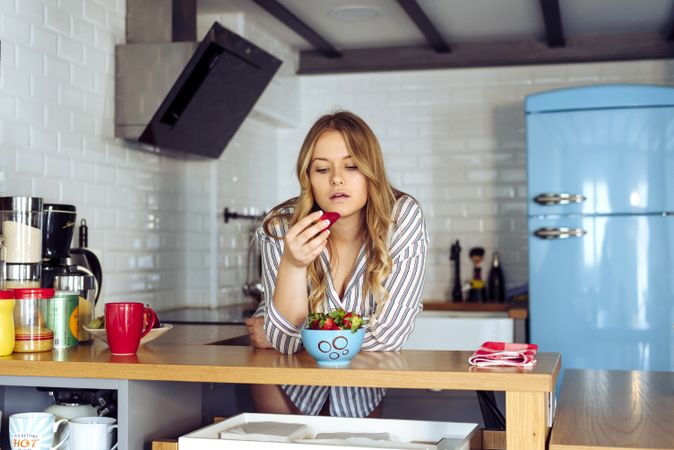 Young seductive female eating strawberry in kitchen