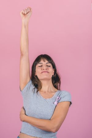 Happy woman wearing a pink breast cancer awareness ribbon is raising her arm showing the struggle with breast cancer