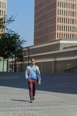 Young bearded man with sunglasses walking on street with hand on pocket