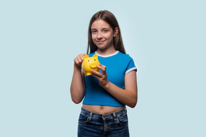 Girl holding yellow piggy bank, smiling.