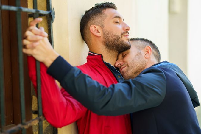 Two men embracing lovingly next to window outside