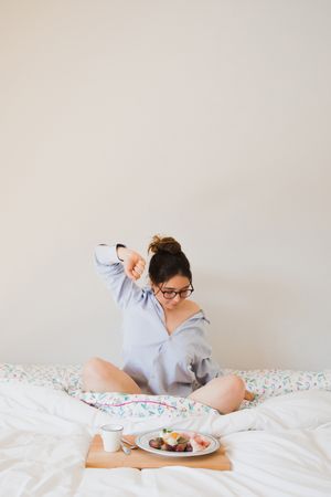 Young woman with breakfast on bed stretching out