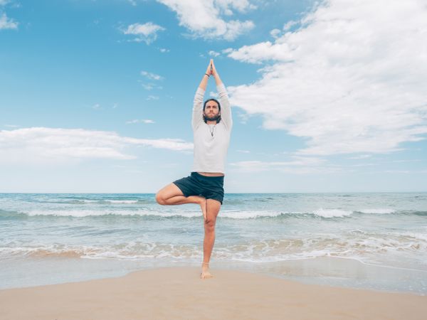 Man training yoga on beach