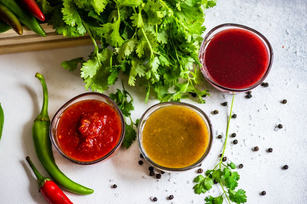 Top view of three traditional Georgian sauces tomato satsebeli, yellow and red tkemali with ingredients on stone background