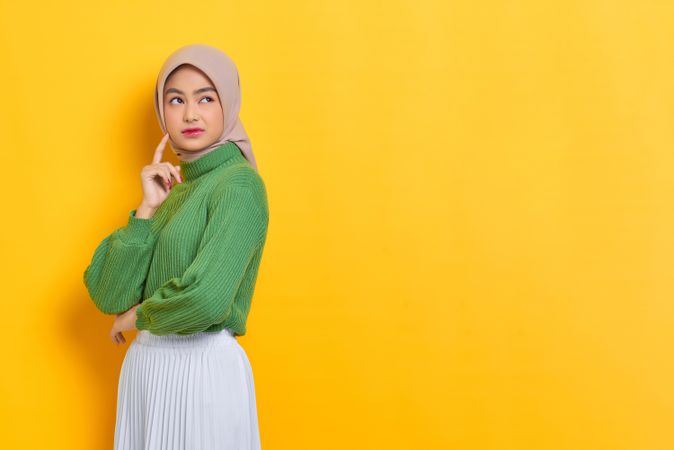 Woman in headscarf looking back thinking about something with one hand on cheek