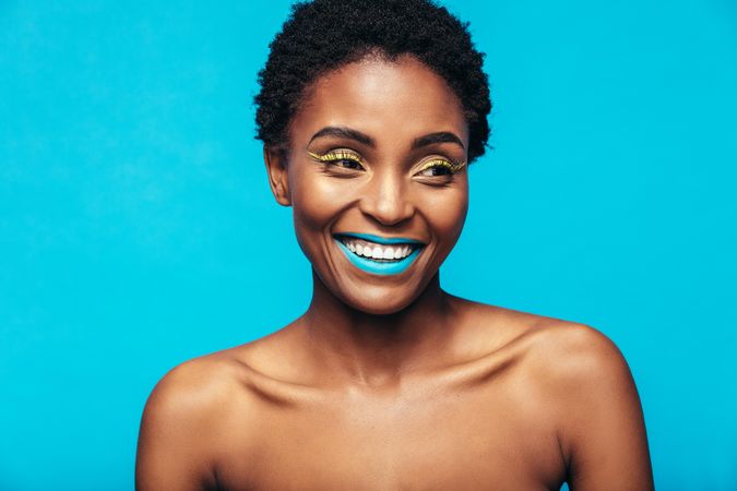 Close up of smiling woman wearing vivid makeup against blue background