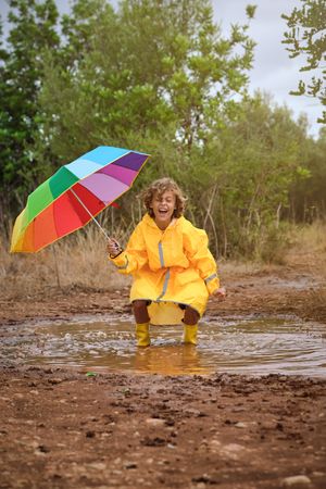 Cheerful boy with umbrella jumping in puddle
