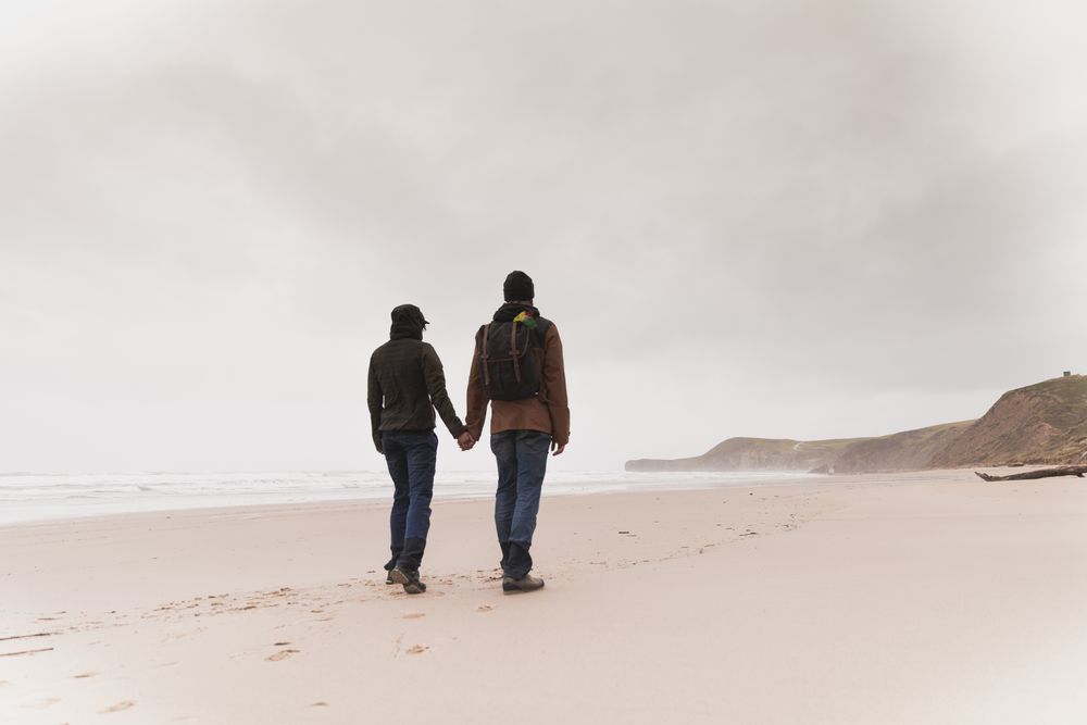 Couple walking on sand shore near water