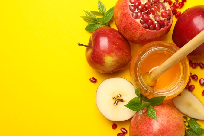 Fresh apples, pomegranate and honey grouped on yellow background