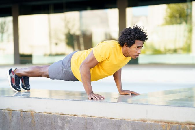 Side view of man doing planks on cement wall outside