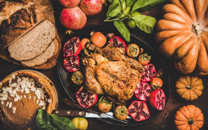 Roasted chicken on table with pomegranates, squash, bread and pie