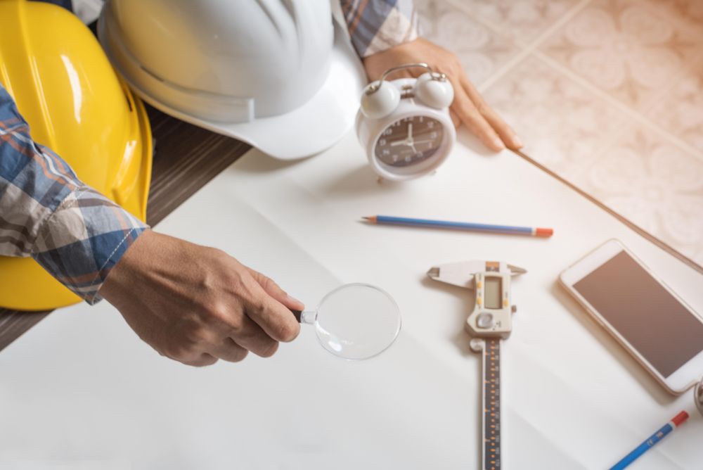 Person at work desk with hard hat, pencils, phone, clock, magnifying glass and calipers
