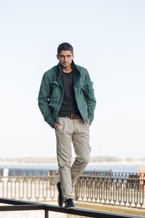 Full body portrait of male in green jacket and slacks walking atop railing