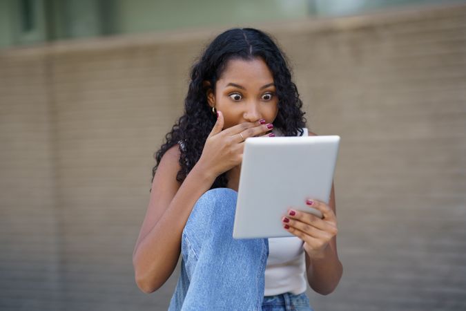 A surprised woman enjoys content on her tablet in a relaxed setting, engaging with joy