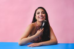 Smiling Hispanic woman with long brown hair holding large make up brush up and looking at camera