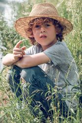 Boy in straw hat relaxing on grass near river