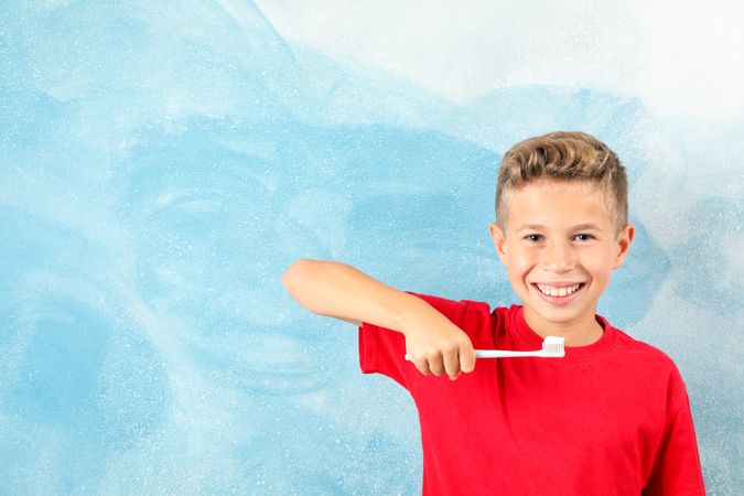 Boy with toothbrush on color background, space for text