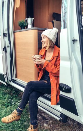 Female relaxing with coffee sitting on camper van step, vertical