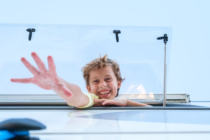 Boy smiling and reaching out from caravan window