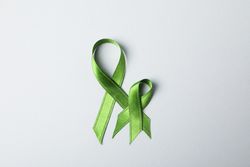 Green awareness ribbons on grey background, space for text