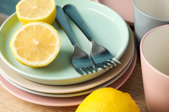 Plates and cups with lemons stacked on wooden table, close up