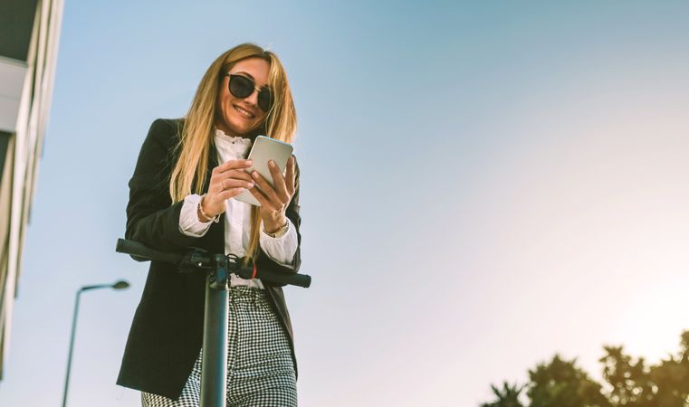 Businesswoman with electric scooter looking at the mobile
