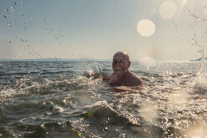 Active older man swimming and splashing in water