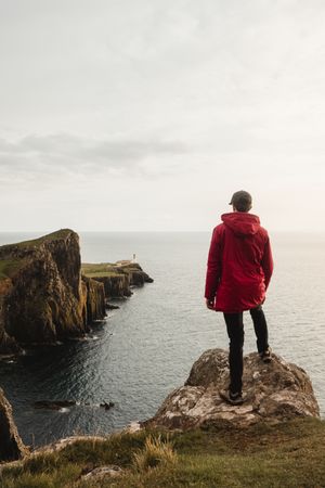 Lonely tourist standing on rocky coast against tranquil sea water under gray sky