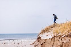 Man walking on sand shore between dry grass near water