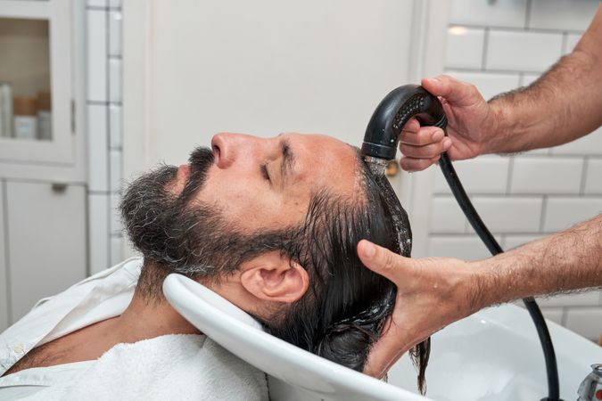 Barber washing hair of bearded male at barbershop