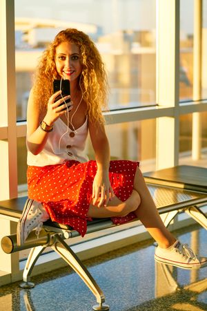Smiling woman sitting on metal bench with earphones and smartphone