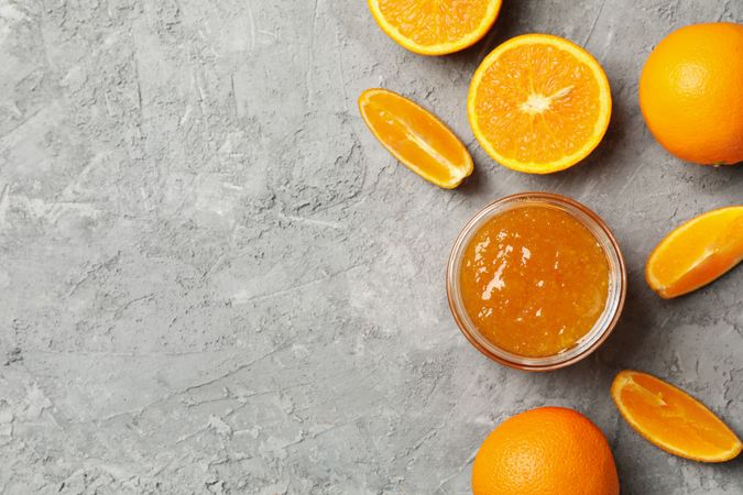 Oranges and glass jar with jam on gray background, top view