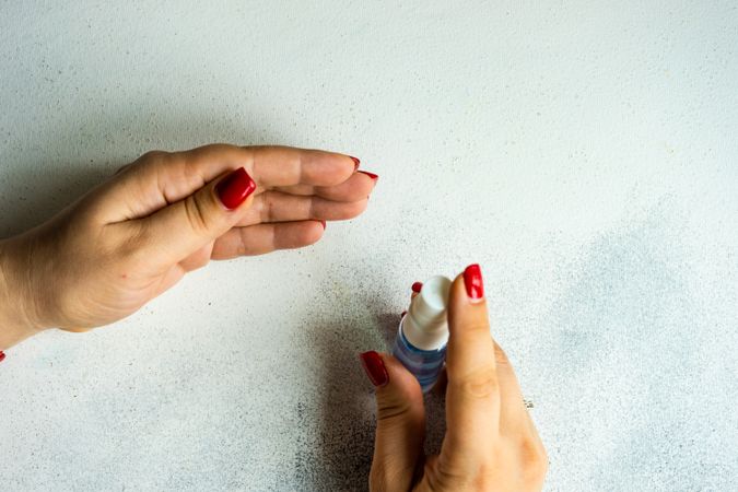 Hands with red nail varnish holding spray bottle