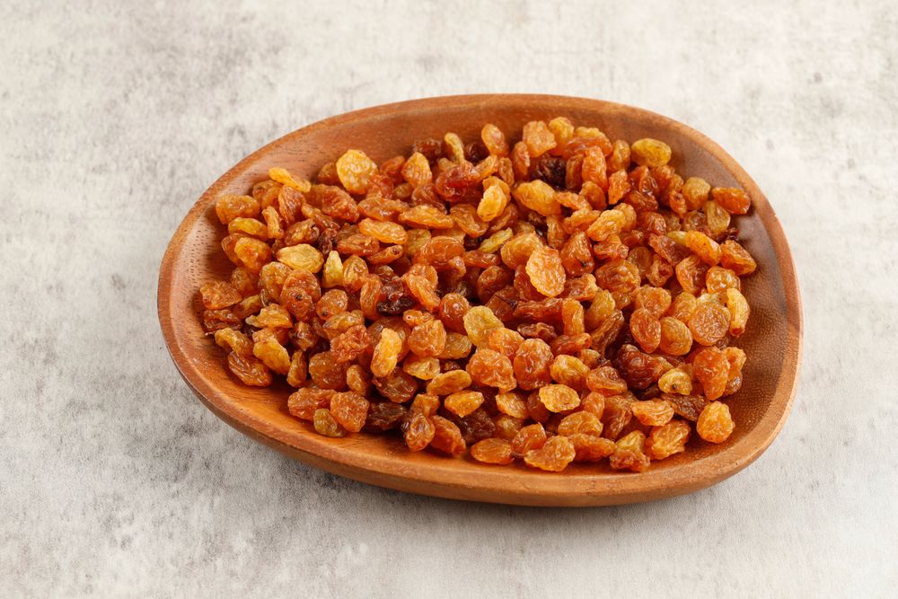 Wooden bowl of golden raisins on marble table