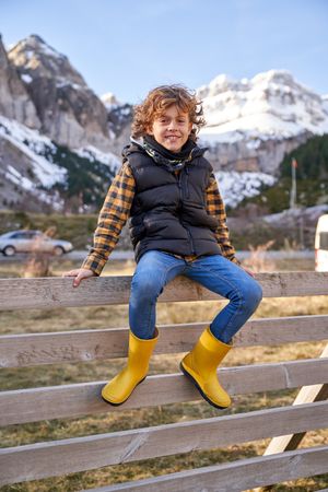 Positive kid sitting on fence in countryside