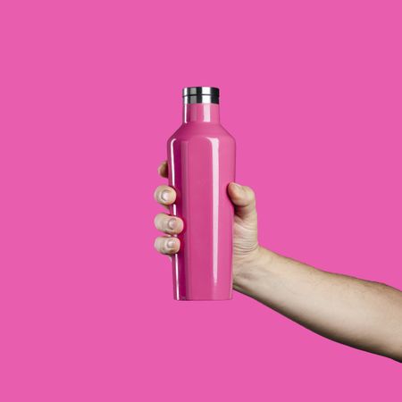Hand holding a pink reusable water bottle on a pink background.