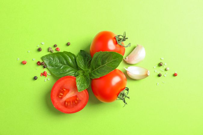 Fresh cherry tomatoes with basil, pepper and garlic on color background, space for text. Ripe vegetables