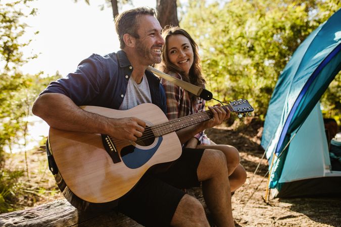 Happy couple playing music with guitar outdoors
