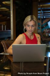 Young woman in red tank top working on laptop in a coffee shop bGQwB5