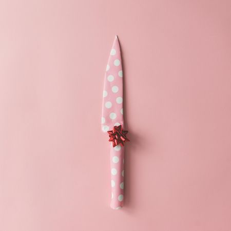 Knife wrapped in dotted paper with bow on pink background