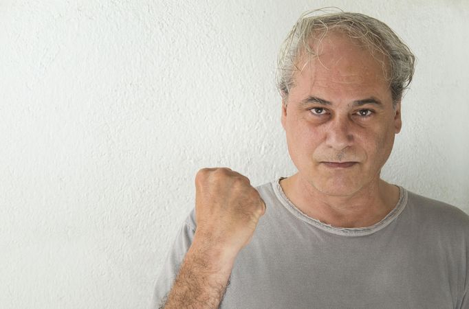 Portrait of angry middle aged man in gray shirt holding a fist