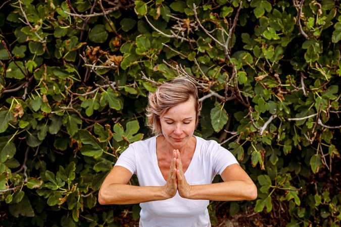 Adult woman meditating near bush