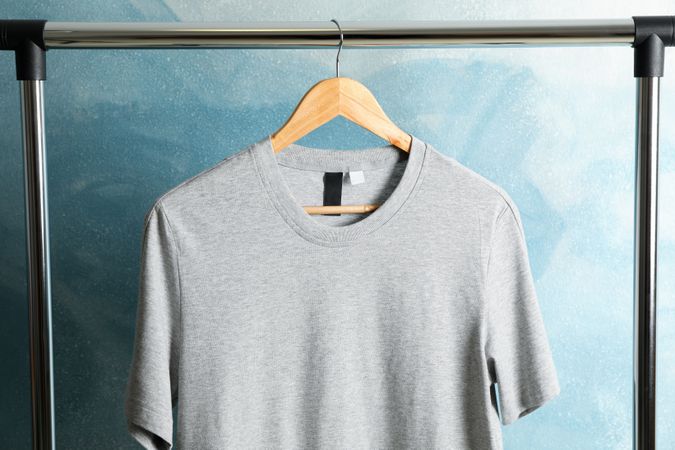 Rack with blank gray t-shirt on blue background, space for text