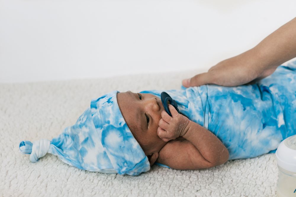 Anonymous mother with newborn baby wrapped on soft blanket with pacifier