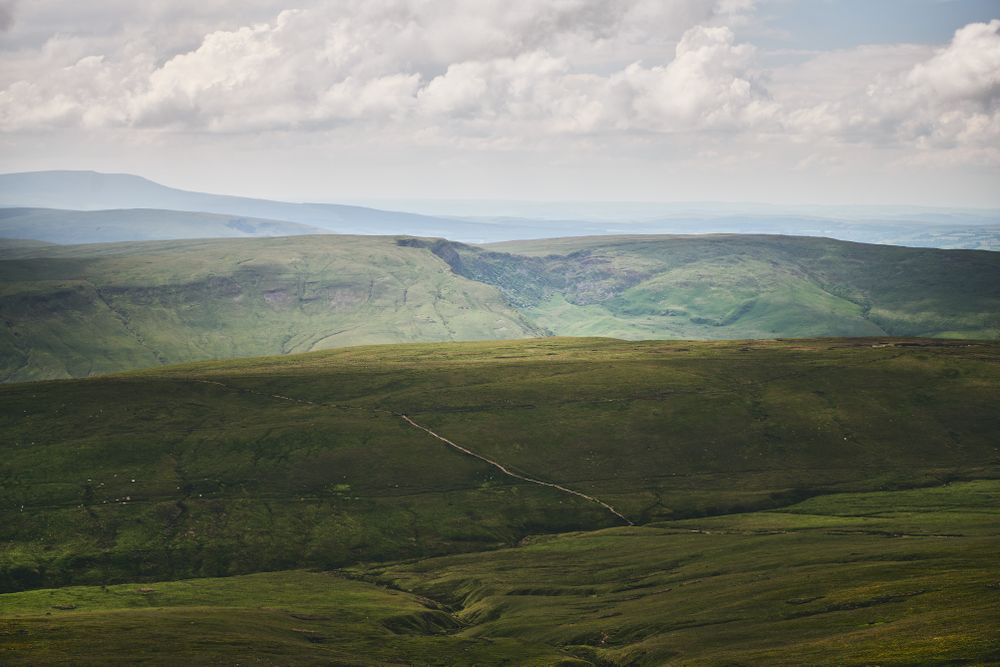 Sun lighting up Brecon Beacons mountain range on an overcast day