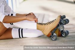 Black woman putting on her roller blades sitting on beach walkway 49oBQ0